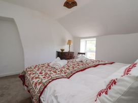 A bedroom with a bed with floral bedding a wooden chest of drawers a lamp and a chair by the window at 2 Beck Houses in Menethorpe near Malton