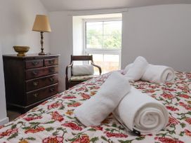 A bedroom with a bed covered by a floral bedspread and rolled white towels a wooden dresser with a lamp and a bowl and a wooden chair by a window at 2 Beck Houses Menethorpe near Malton
