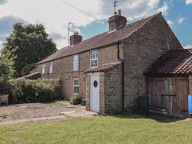 A stone house with a tiled roof and white door with grassy yard at 2 Beck Houses in Menethorpe near Malton