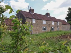 A stone cottage with a tiled roof and chimney stacks with green plants and grass in the foreground at 2 Beck Houses in Menethorpe near Malton