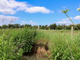 A grassy field with shrubs and a small water body under a blue sky at 2 Beck Houses in Menethorpe near Malton