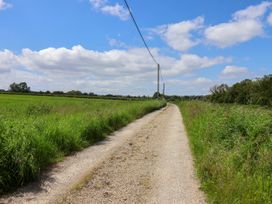 A gravel road with green grass and utility poles on both sides under a blue sky at 2 Beck Houses in Menethorpe near Malton