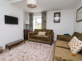 A living room with two brown sofas and patterned cushions a rug and a wall mounted tv at 2 Beck Houses in Menethorpe near Malton