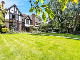 A large garden with a manicured lawn and trees in front of a Tudor style house at Tudor Grange in Bournemouth