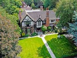 A large house with a tiled roof and black and white exterior surrounded by trees and a lawn with a stone path and outdoor chairs at Tudor Grange in Bournemouth