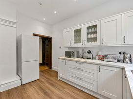 A kitchen with white cabinets wooden floor and various appliances including a refrigerator microwave toaster and kettle at Tudor Grange in Bournemouth