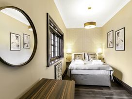 A bedroom with a bed two bedside lamps two framed pictures a round mirror and a wooden desk at Tudor Grange in Bournemouth