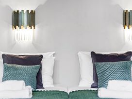 Two beds with white sheets and pillows each with a dark pillow and a green patterned cushion under wall lights at Tudor Grange in Bournemouth