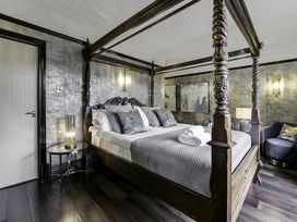 A bedroom with a four-poster bed bedside tables lamps armchair and wall art at Tudor Grange in Bournemouth