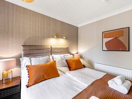 A bedroom with a double bed two orange pillows two bedside tables with lamps and abstract wall art at Tudor Grange in Bournemouth