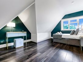A bedroom with a bed beside a window and a desk with a lamp and stool under a sloped ceiling at Tudor Grange in Bournemouth