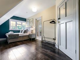 A bedroom with a bed, nightstand with lamp, window, clothes rack, and a door leading to a bathroom at Tudor Grange in Bournemouth