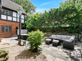 An outdoor patio with wicker furniture including a sofa and stools a hot tub a stone bench a street lamp and trees at Tudor Grange in Bournemouth