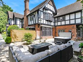 An outdoor patio with cushioned seating a glass table hot tub and a timber framed house at Tudor Grange in Bournemouth