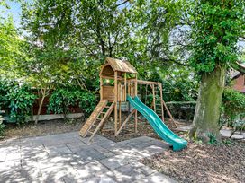 A wooden playset with a slide and climbing features in a garden with trees at Tudor Grange in Bournemouth