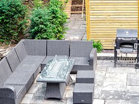 An outdoor patio area with a grey wicker corner sofa a glass table two small stools a barbecue grill and wooden fence at Tudor Grange in Bournemouth