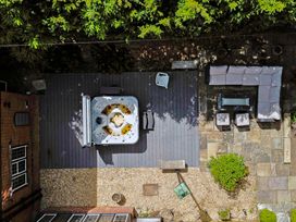 An outdoor area with a hot tub on wooden decking a patio with L shaped sofa stools and a fire pit at Tudor Grange in Bournemouth