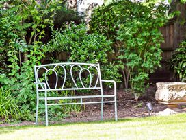 A metal garden bench and a stone planter among green bushes in a backyard at Tudor Grange in Bournemouth