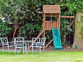 A backyard with a wooden playset including a slide and swing and a metal table with four chairs on grass at Tudor Grange in Bournemouth