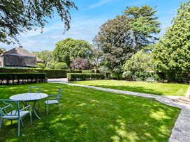 A garden with a round table and four chairs on the grass and a paved pathway at Tudor Grange in Bournemouth