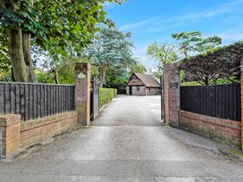 An open driveway gate with brick pillars leading to a parking area and a small brick building surrounded by trees at Tudor Grange in Bournemouth