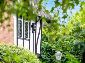 A black and white timber framed house partly covered by green foliage with a street lamp and trees in the background at Tudor Grange in Bournemouth