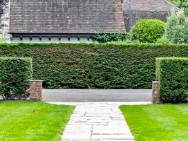 A garden pathway with green grass and hedges leading to a driveway and a house roof in the background at Tudor Grange in Bournemouth