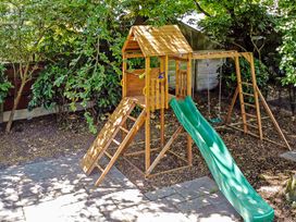 A wooden play structure with a slide and swings in a garden at Tudor Grange in Bournemouth
