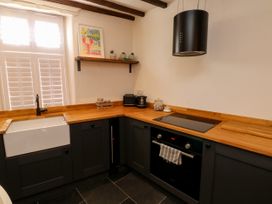 A kitchen with wooden countertops black cabinets a white sink a stove oven and a shelf with decorations at The Nook in Brixham
