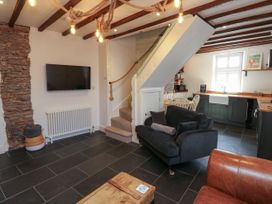 A living area with a wall-mounted TV a staircase a black sofa a dining table and a kitchen with a window at The Nook in Brixham
