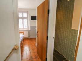 A bedroom with wooden floor and a bed visible through a door with a bathroom with green tiled walls next to it at The Nook in Brixham