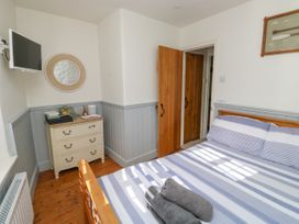 A bedroom with a wooden bed striped bedding and folded towels a chest of drawers a wall-mounted tv and an open wooden door at The Nook in Brixham