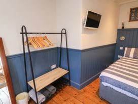 A bedroom corner with a bed a wall-mounted TV a clothes rack with hangers and folded towels on a wooden floor at The Nook in Brixham