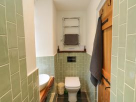 A small bathroom with a toilet a sink on a wooden countertop green wall tiles and a wooden door at The Nook in Brixham