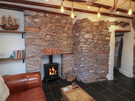 A living room with a stone fireplace wood stove leather sofa shelves with books and a model ship at The Nook in Brixham