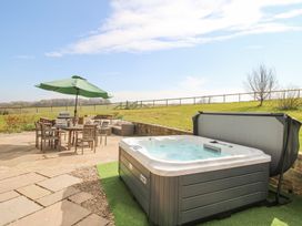 An outdoor patio area with a hot tub wooden table with umbrella chairs and garden seating at Cuckoo Pen Cottage in Eastham near Tenbury Wells