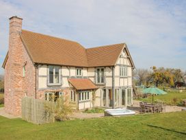 An exterior view of a two-story house with a patio area including a table with chairs and an umbrella and a hot tub in a grassy yard at Cuckoo Pen Cottage Eastham near Tenbury Wells