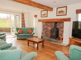 A living room with green sofas a wooden coffee table wood burning stove and an open door to a garden at Cuckoo Pen Cottage Eastham near Tenbury Wells