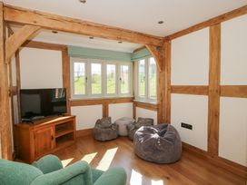 A room with wooden beams a TV on a wooden stand bean bags and windows showing outside at Cuckoo Pen Cottage in Eastham near Tenbury Wells