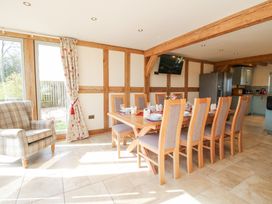 A dining room with a wooden table set for eight chairs and a plaid armchair at Cuckoo Pen Cottage in Eastham near Tenbury Wells