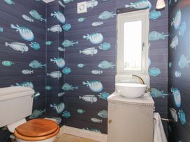 A bathroom with a toilet and a sink under a window with fish patterned wallpaper at Cuckoo Pen Cottage in Eastham near Tenbury Wells