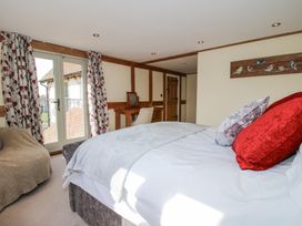 A bedroom with a bed red and silver pillows a chair and a desk near French doors with floral curtains at Cuckoo Pen Cottage in Eastham near Tenbury Wells