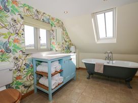 A bathroom with a clawfoot bathtub a wooden toilet seat a blue vanity with rolled towels and floral wallpaper at Cuckoo Pen Cottage Eastham near Tenbury Wells