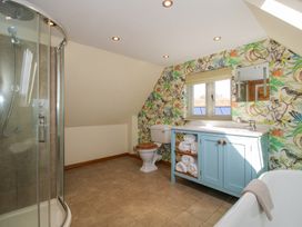 A bathroom with a curved glass shower cubicle a toilet with wooden seat a blue cabinet with rolled towels a sink and a bathtub with a towel at Cuckoo Pen Cottage Eastham near Tenbury Wells