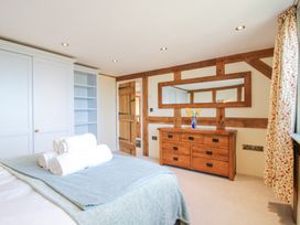 A bedroom with a bed, folded towels, wooden dresser with a vase, large mirror, wooden door, built-in white wardrobe, and floral curtains at Cuckoo Pen Cottage in Eastham near Tenbury Wells
