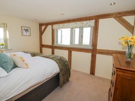 A bedroom with a bed cushions and a blanket a wooden dresser with a vase of flowers and windows with floral blinds at Cuckoo Pen Cottage in Eastham near Tenbury Wells