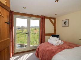 A bedroom with a bed covered by a red blanket and white towels near double glass doors showing a grassy outdoor area at Cuckoo Pen Cottage in Eastham near Tenbury Wells