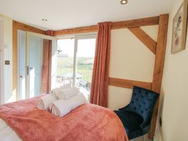 A bedroom with a bed covered by a pink blanket and rolled white towels on it next to a blue chair and open doors leading to a balcony with a view of green fields at Cuckoo Pen Cottage in Eastham near Tenbury Wells