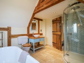 A bathroom with a bathtub a toilet a sink on a blue vanity a wooden door and a glass shower with patterned tiles at Cuckoo Pen Cottage in Eastham near Tenbury Wells
