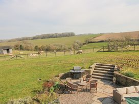 An outdoor patio area with chairs a table and a barbecue overlooking a fenced field with sheep at Cuckoo Pen Cottage in Eastham near Tenbury Wells